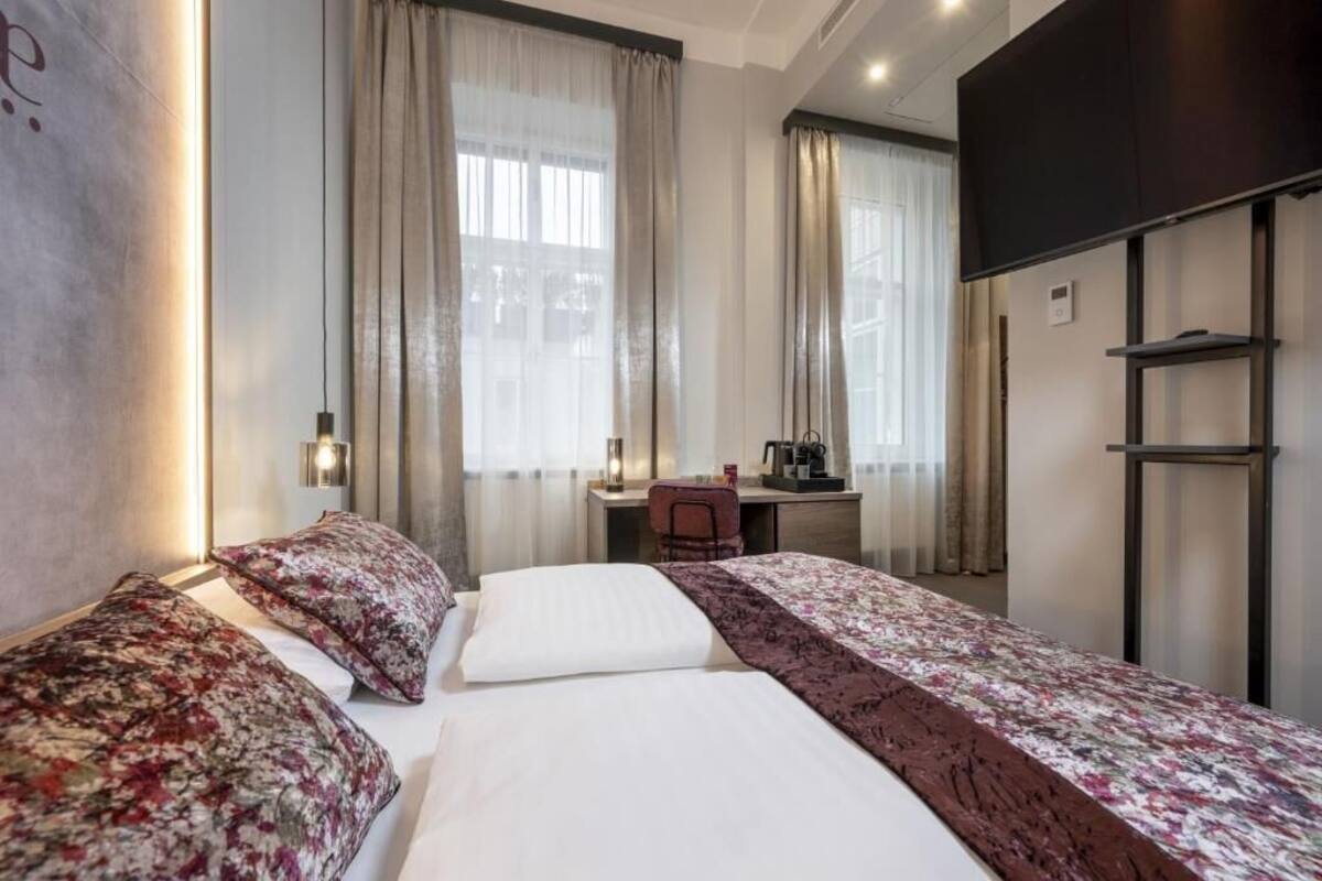A hotel room with two beds, a desk, a TV, and a coffee machine.