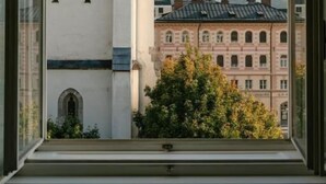 A window with a view of a building with a clock tower and another building with a red facade. - HOTEL andrä (Salzburg)