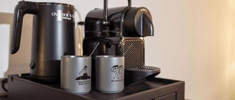 A coffee maker, a kettle, and two cans on a tray.
