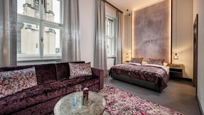 A hotel room with a large bed, a sofa, a round coffee table, and a cityscape view through large windows. - HOTEL andrä (Salzburg)