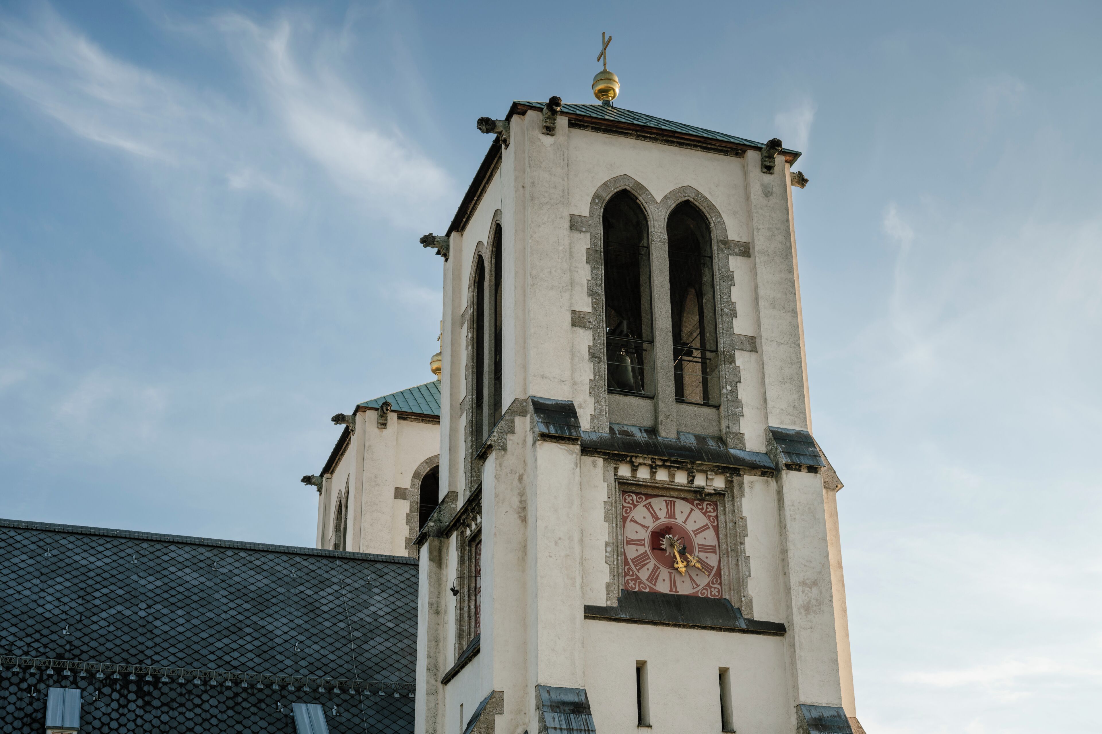Una torre de iglesia con un reloj, ventanas arqueadas y un veleta.
