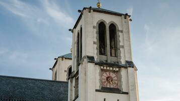 Una torre de iglesia con un reloj, ventanas arqueadas y un veleta.