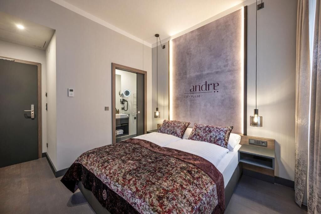 Una habitación de hotel con cama, tocador con espejo, lámpara de pared y una puerta.