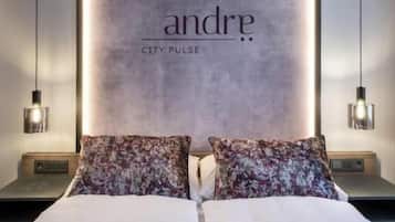 Una cama con almohadas florales, una pared grande con el texto 'andre CITY PULSE', y lámparas colgantes.