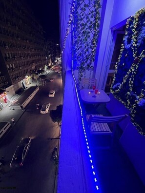 A balcony with a view of a street at night, featuring a table and chairs, and decorative plants. - Downtown view studios (Cairo)