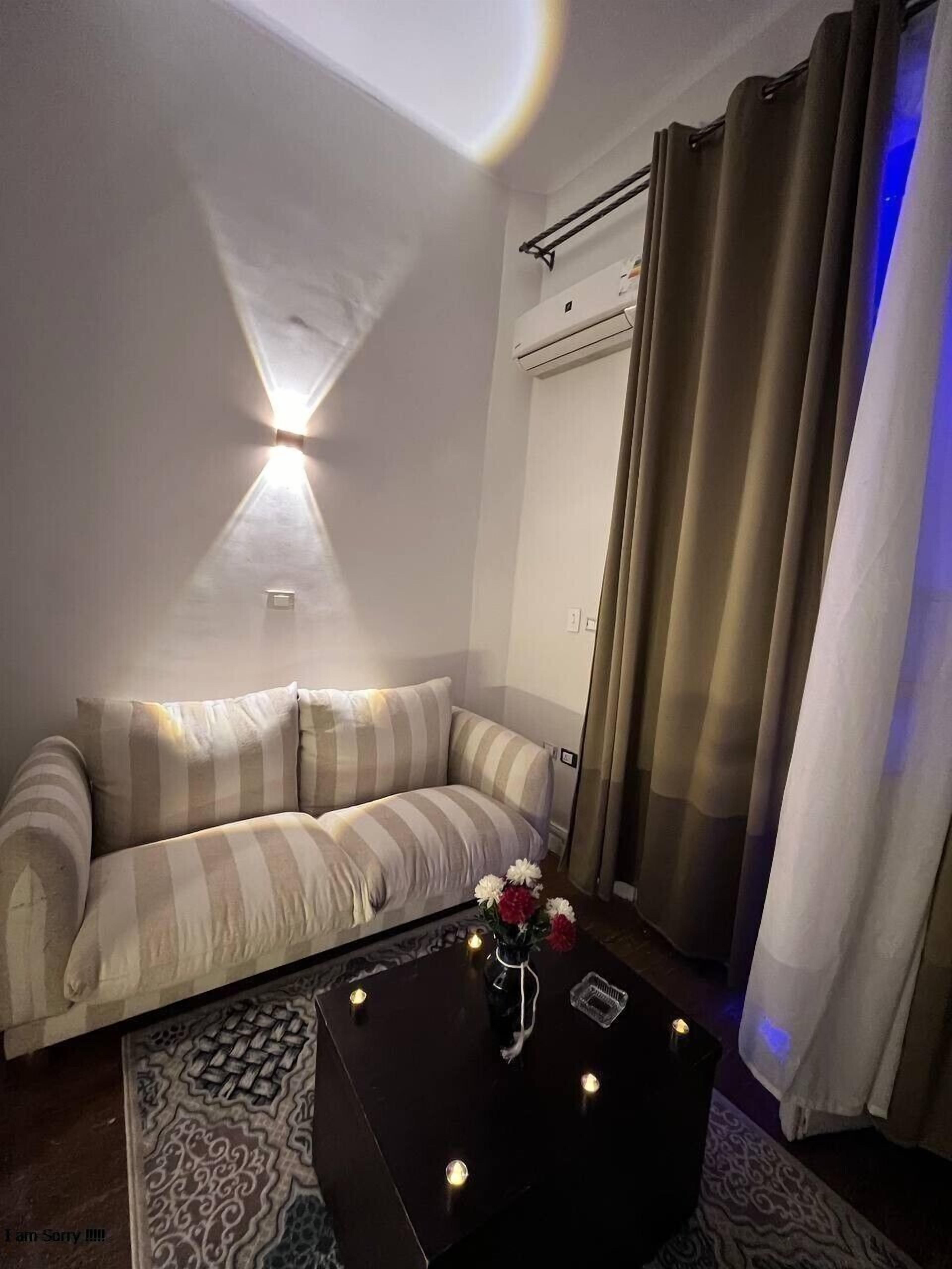 Een moderne woonkamer met een gestreept bankje, een bijzettafeltje met kaarsen en uitzicht naar buiten door een raam met gordijnen.