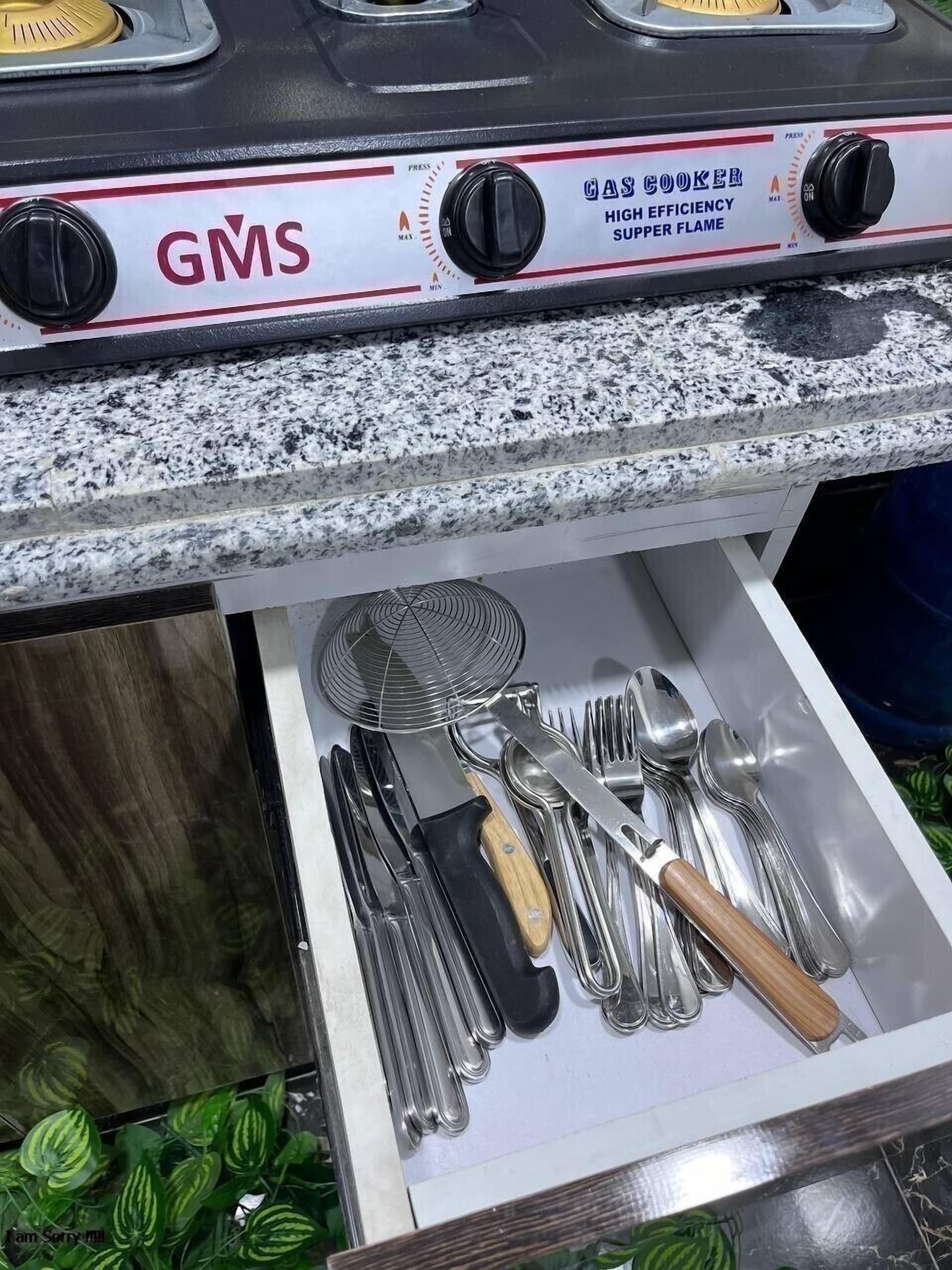 A kitchen area with a GMS branded stove, a drawer containing various utensils, and a granite countertop.