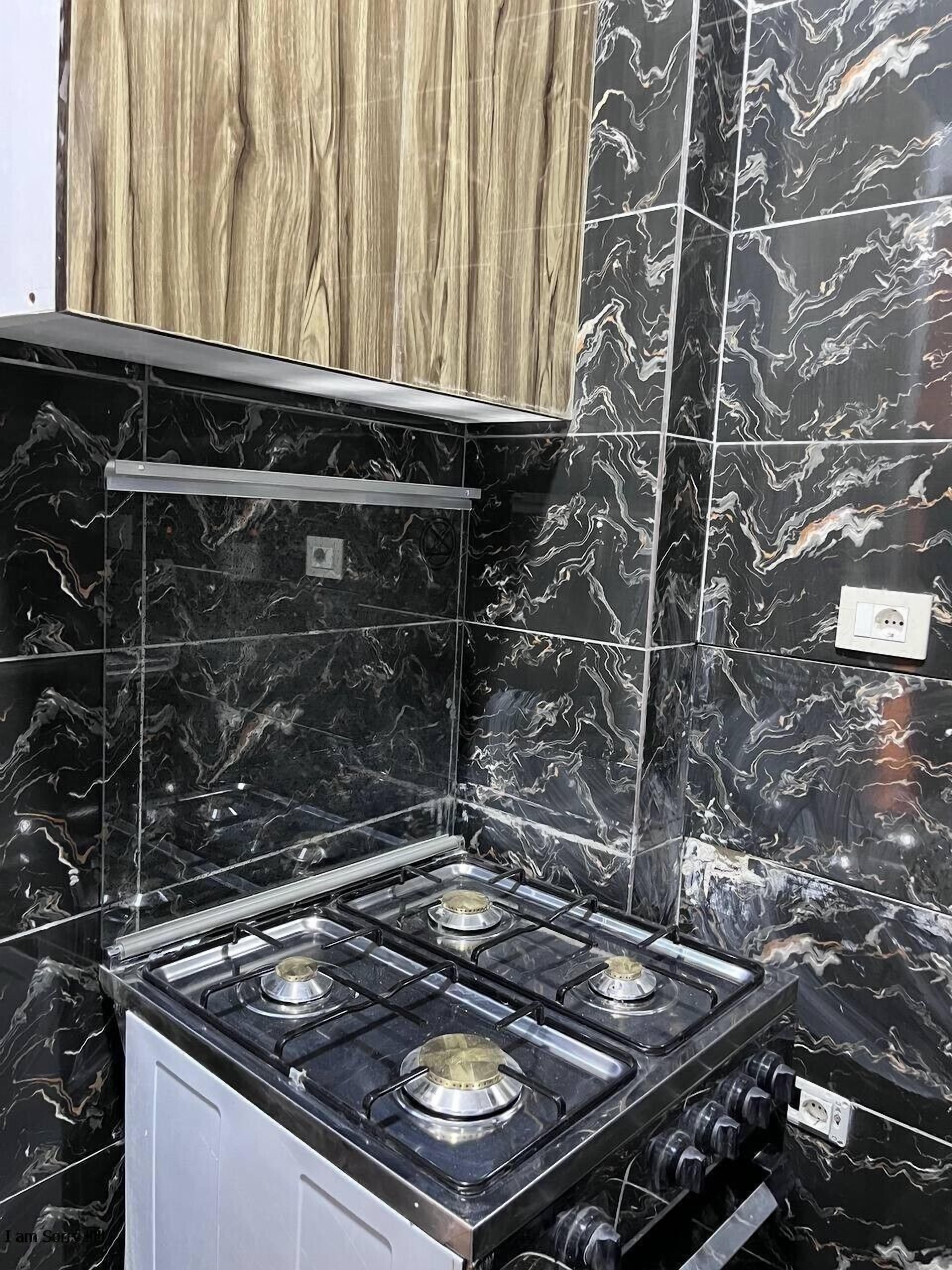 A kitchen with black marble tiles, a gas stove, and wooden cabinets.