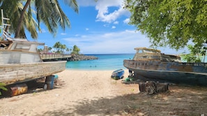 Dos barcos en una playa arenosa con cielo azul despejado y mar tranquilo.
