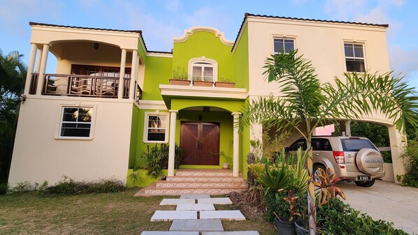 Una casa de dos pisos con fachada verde y beige, un balcón y un SUV estacionado.