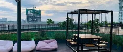 Une terrasse sur le toit avec un fauteuil suspendu, un espace salon et une vue sur un chantier de construction.
