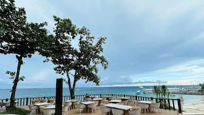 Un restaurant en bord de mer avec une terrasse, une plateforme en bois et une vue sur l’océan et les bateaux.