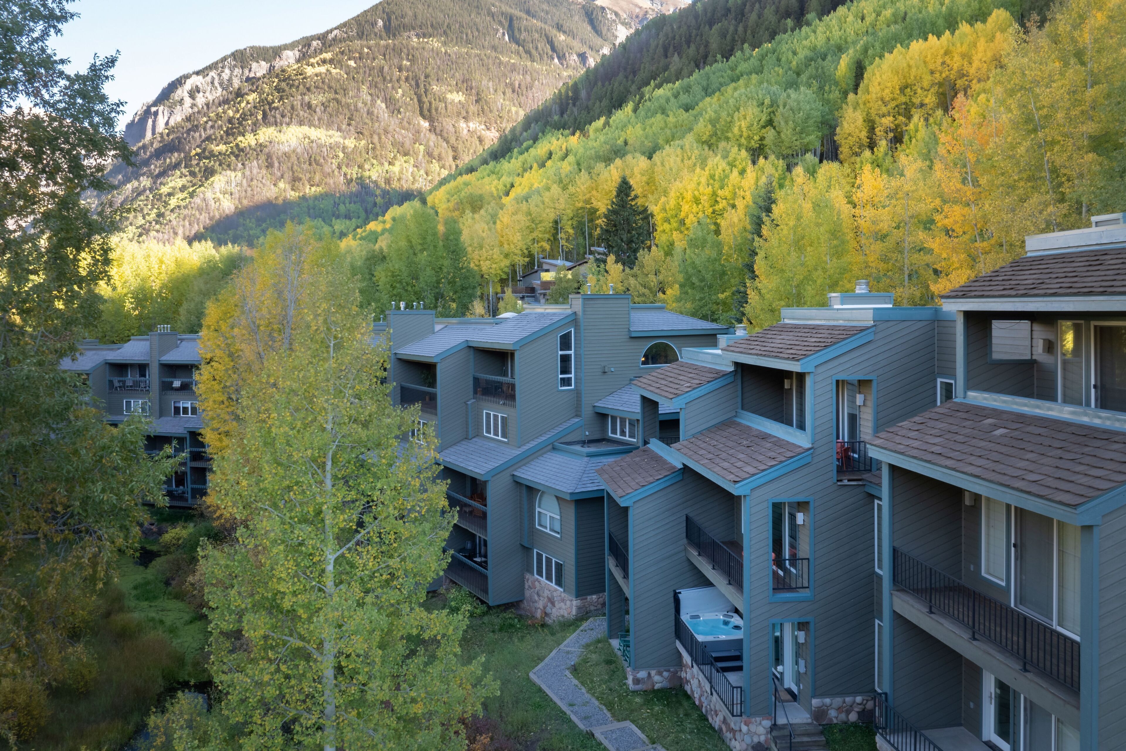 Un immeuble à plusieurs étages doté de balcons, d’une piscine et offrant une vue sur une montagne boisée.