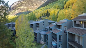 Un immeuble à plusieurs étages doté de balcons, d’une piscine et offrant une vue sur une montagne boisée.