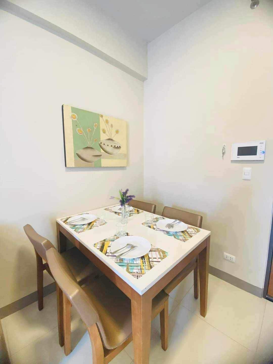 A dining area with a table set for four, a vase with flowers, and a wall-mounted thermostat.