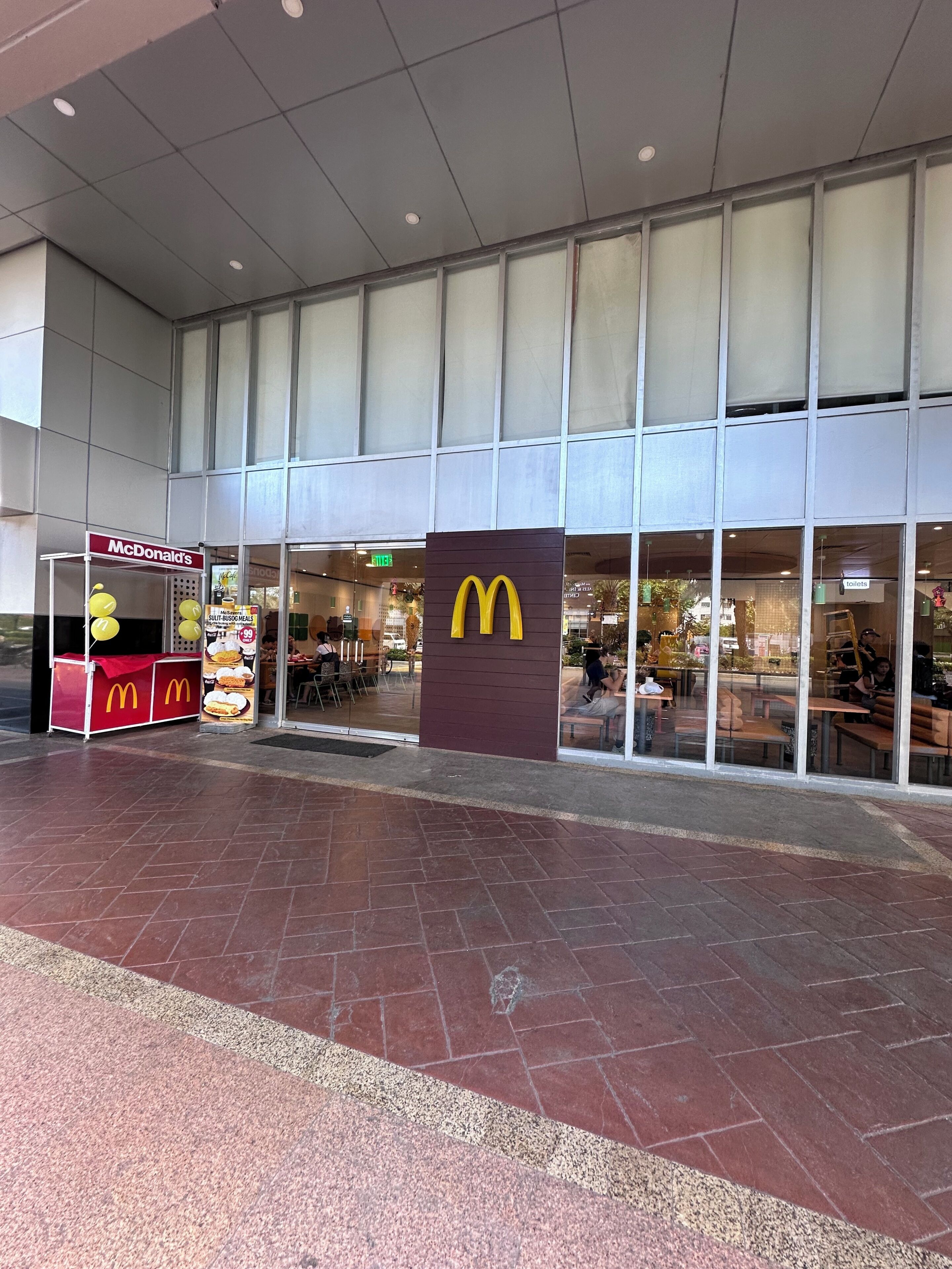 Un restaurant McDonald's avec un grand logo, des places assises à l'extérieur et un espace d'entrée carrelé.