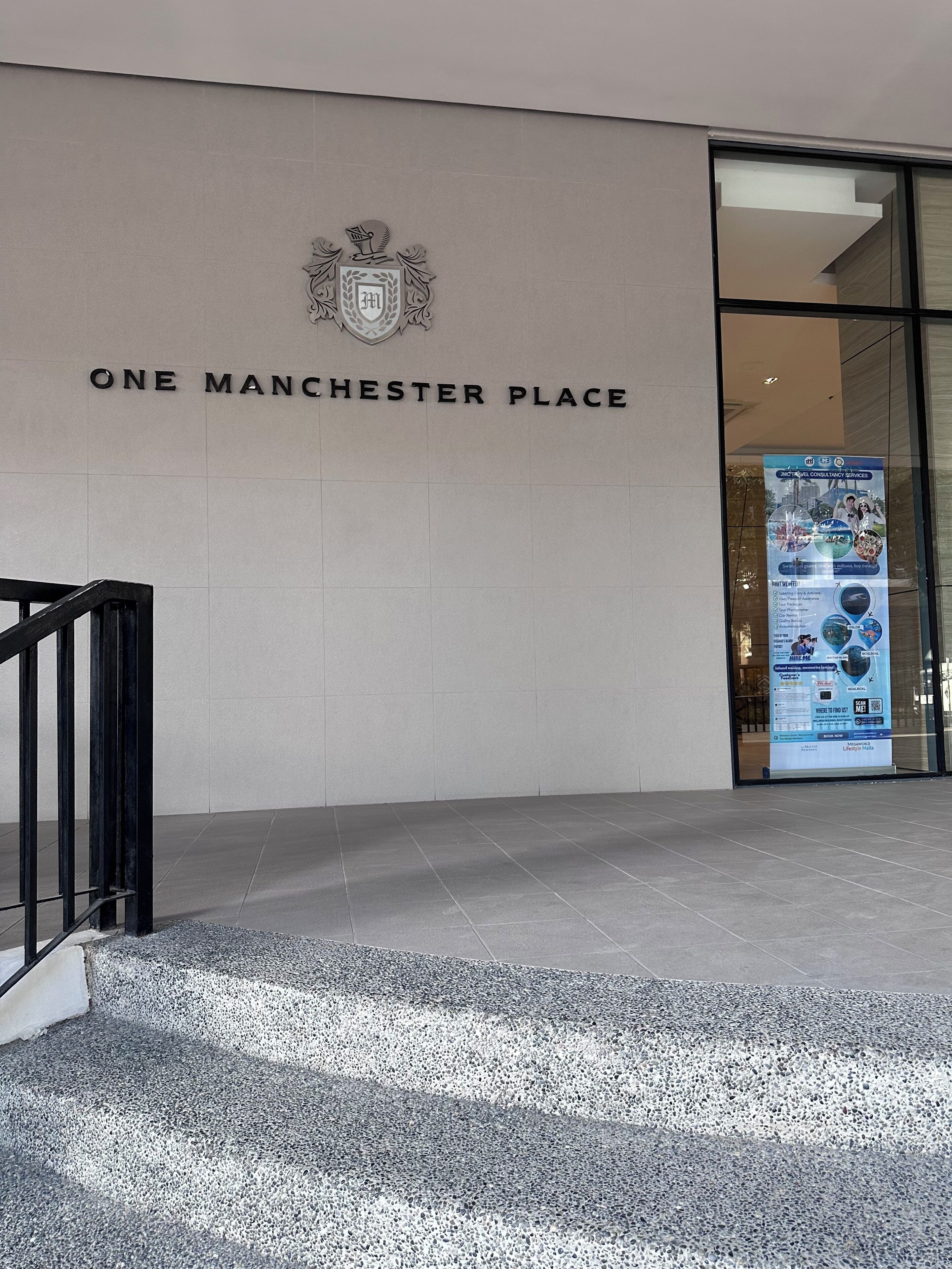 Ein Gebäudeeingang mit einem Schild, auf dem 'ONE MANCHESTER PLACE' steht, und einem Wappen darüber.