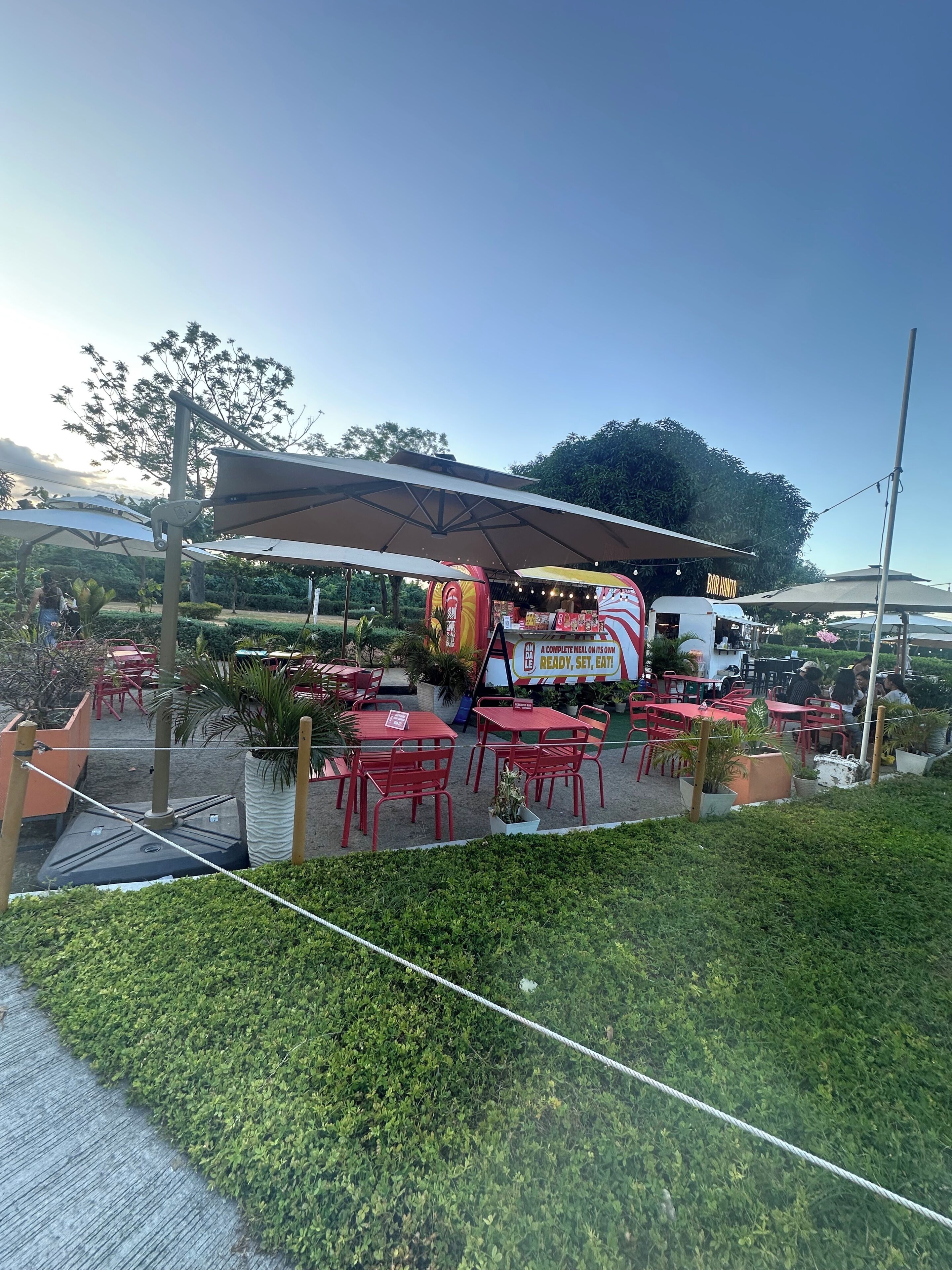 An outdoor dining area with tables and chairs, a covered seating area, and a food truck.