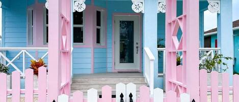 A pink and white wooden gate with a porch leading to a blue house.