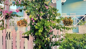 A garden with a pink fence, a pergola, and a blue building with white chairs. - Rest Ashore, BRAND NEW 2-bedroom cottage in Spanish Wells!FREE golfcart (Spanish Wells)