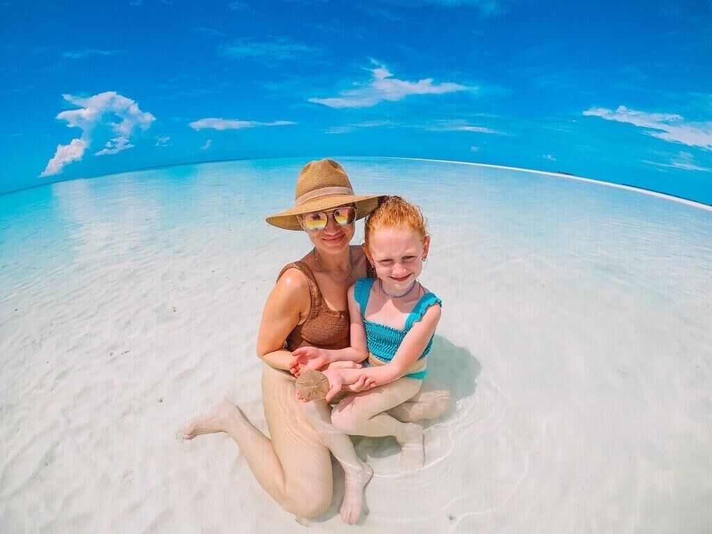 Un couple est assis sur une plage, avec une eau et un ciel d’un bleu limpide.