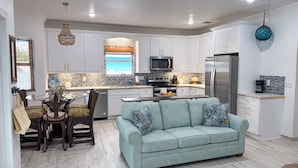 A modern kitchen with white cabinetry, a central island, and a dining area with a table and chairs. - Rest Ashore, BRAND NEW 2-bedroom cottage in Spanish Wells!FREE golfcart (Spanish Wells)
