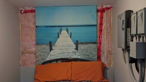 Ein Schlafzimmer mit einem Bett, einem Wandheizkörper und einem Gemälde von einem Steg, der zu einem Strand führt.