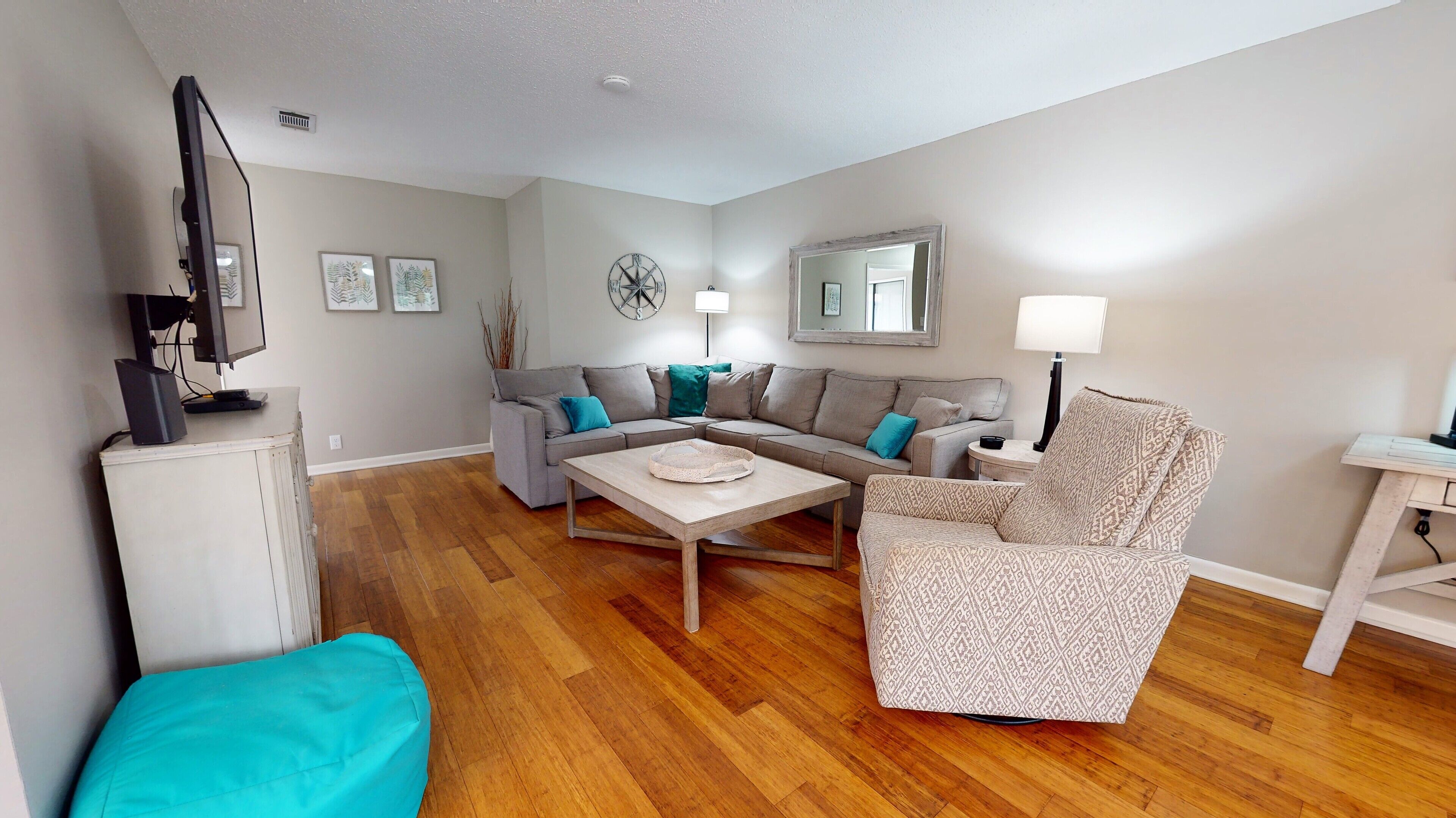 A living room with a grey sofa, a patterned armchair, a coffee table, and a TV on a stand.