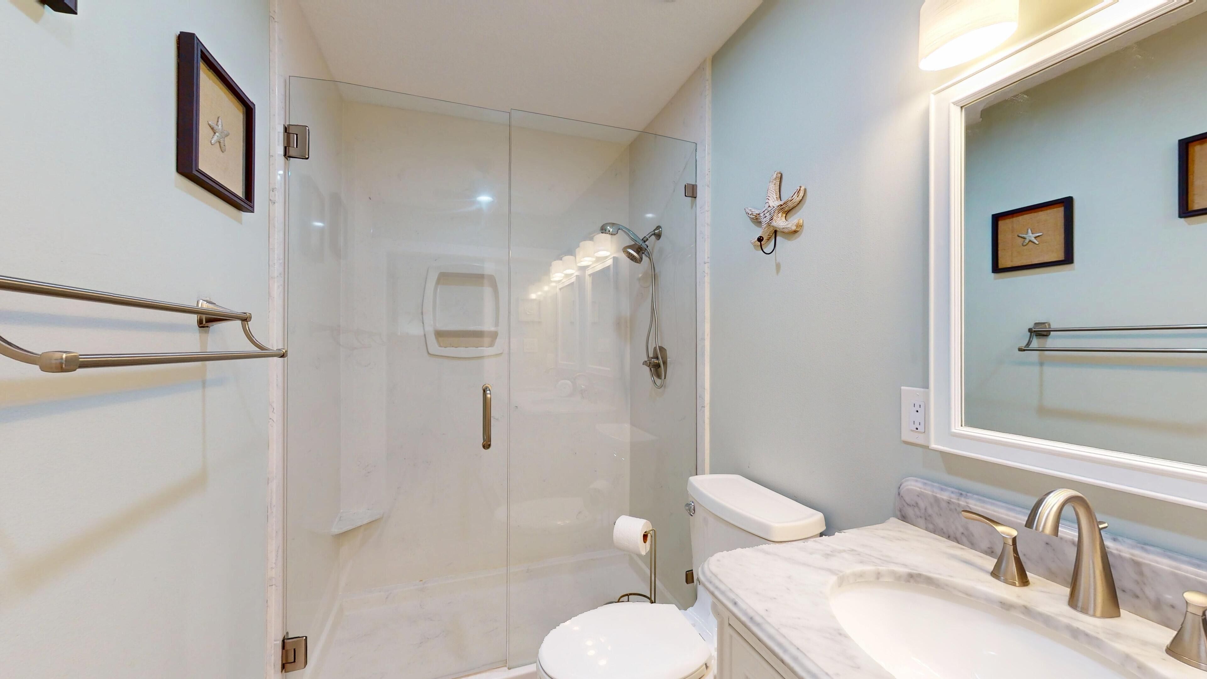 A bathroom with a glass-enclosed shower, a toilet, and a sink with a marble countertop.