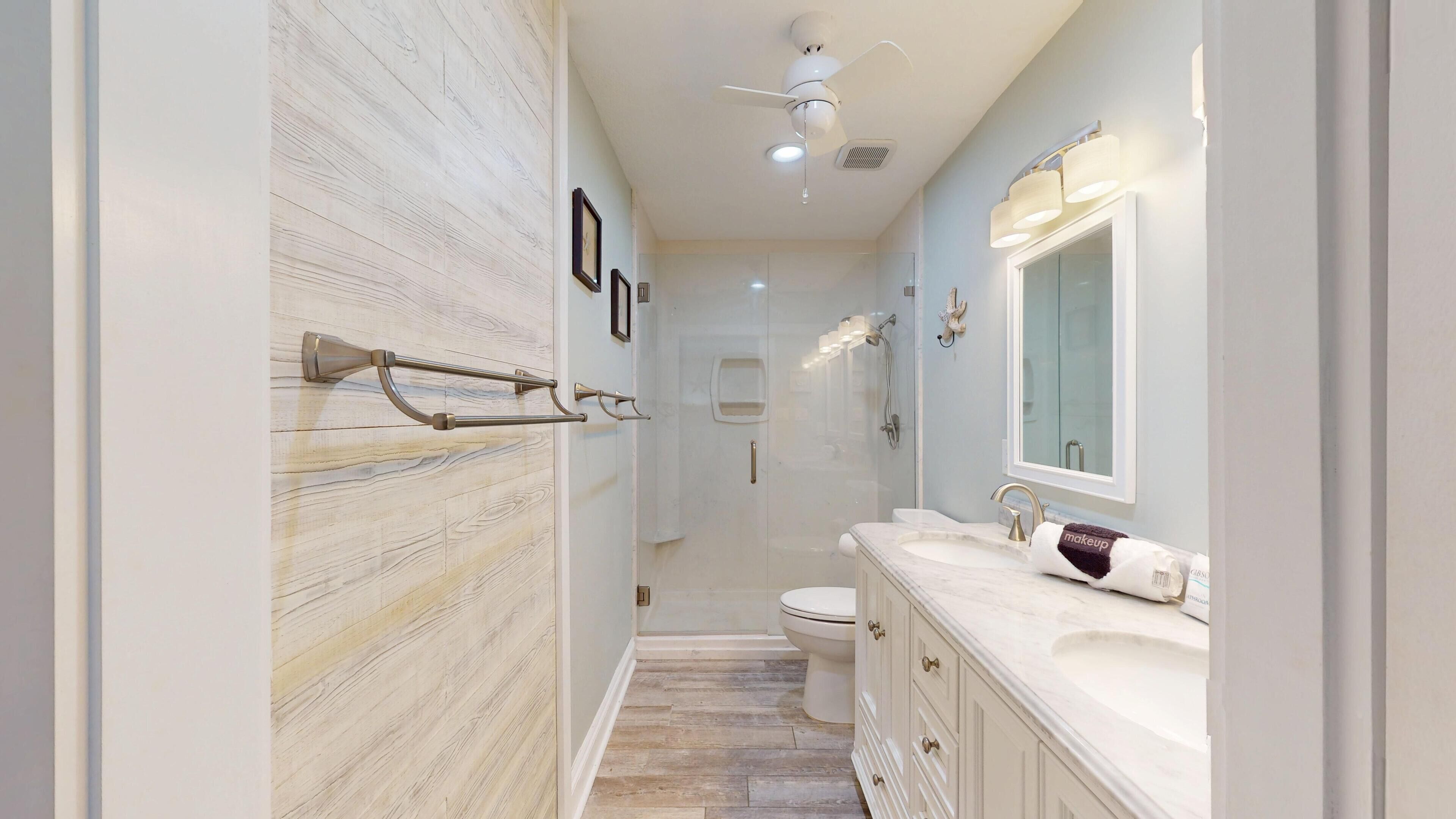A modern bathroom with a marble wall, a large mirror, a vanity with a sink, and a toilet.