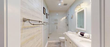 A modern bathroom with a marble wall, a large mirror, a vanity with a sink, and a toilet.