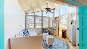 A room with a white sofa, a patterned armchair, a small table, and a blue patterned rug. There is a ceiling fan, a window with blinds, and a door with a turquoise frame. - Augusta Village Sandestin by Gibson BR  (Miramar Beach)