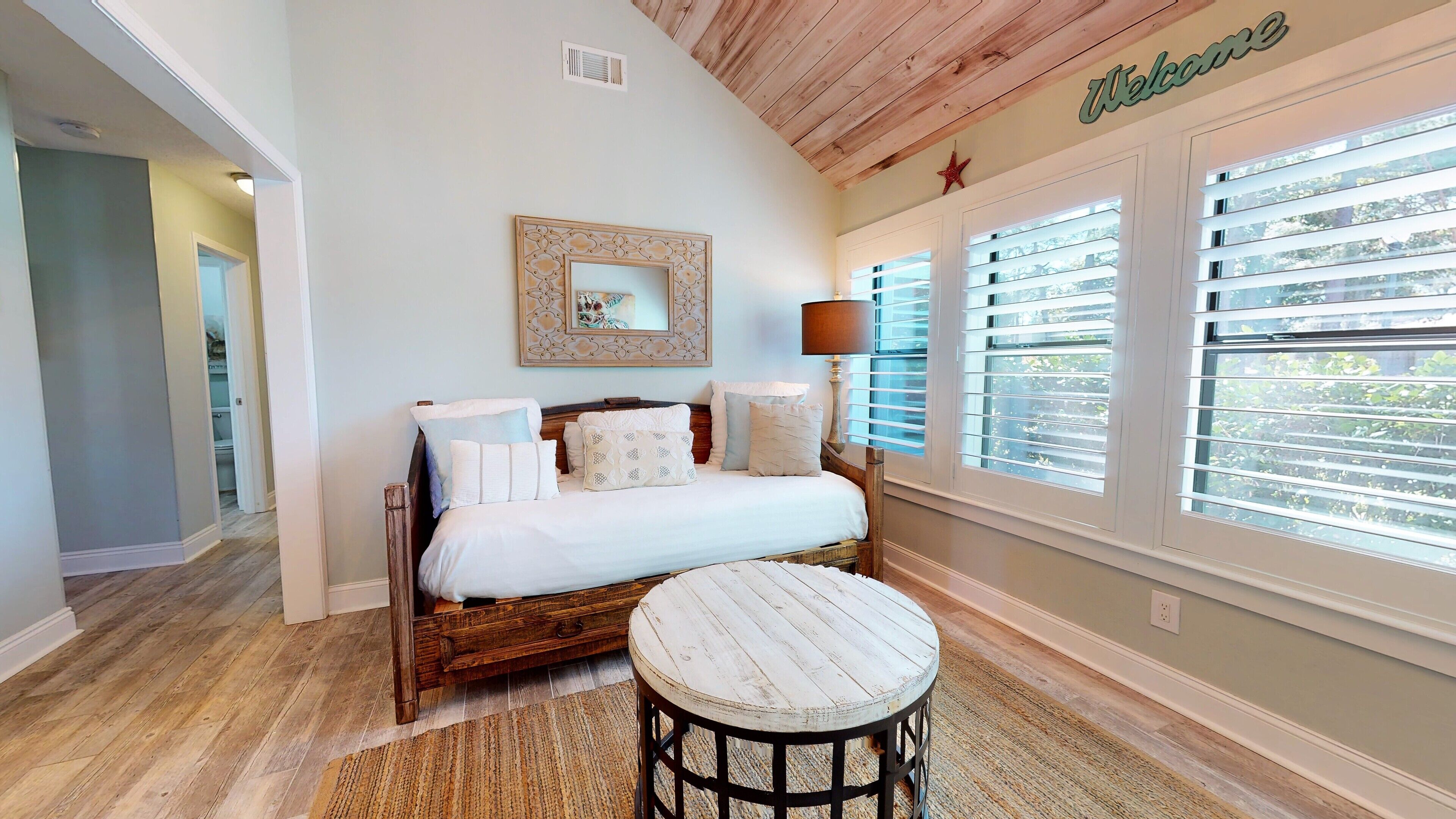 A bedroom with a wooden bed, a bedside table, a rug, and a window with blinds.