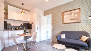 A modern kitchen with white cabinets, a dining table with chairs, and a dark-colored sofa in a living area with patterned wallpaper and a mirror. - Home Chic Home Les Toits de l'Argenterie (Montpellier)