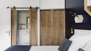 A bedroom with a bed, wooden closet doors, a mirror, and a small shelf with toiletries. - Home Chic Home Les Toits de l'Argenterie (Montpellier)
