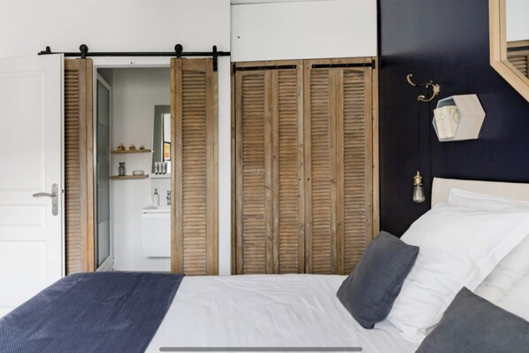 A bedroom with a bed, wooden closet doors, a mirror, and a small shelf with toiletries. - Home Chic Home Les Toits de l'Argenterie (Montpellier)