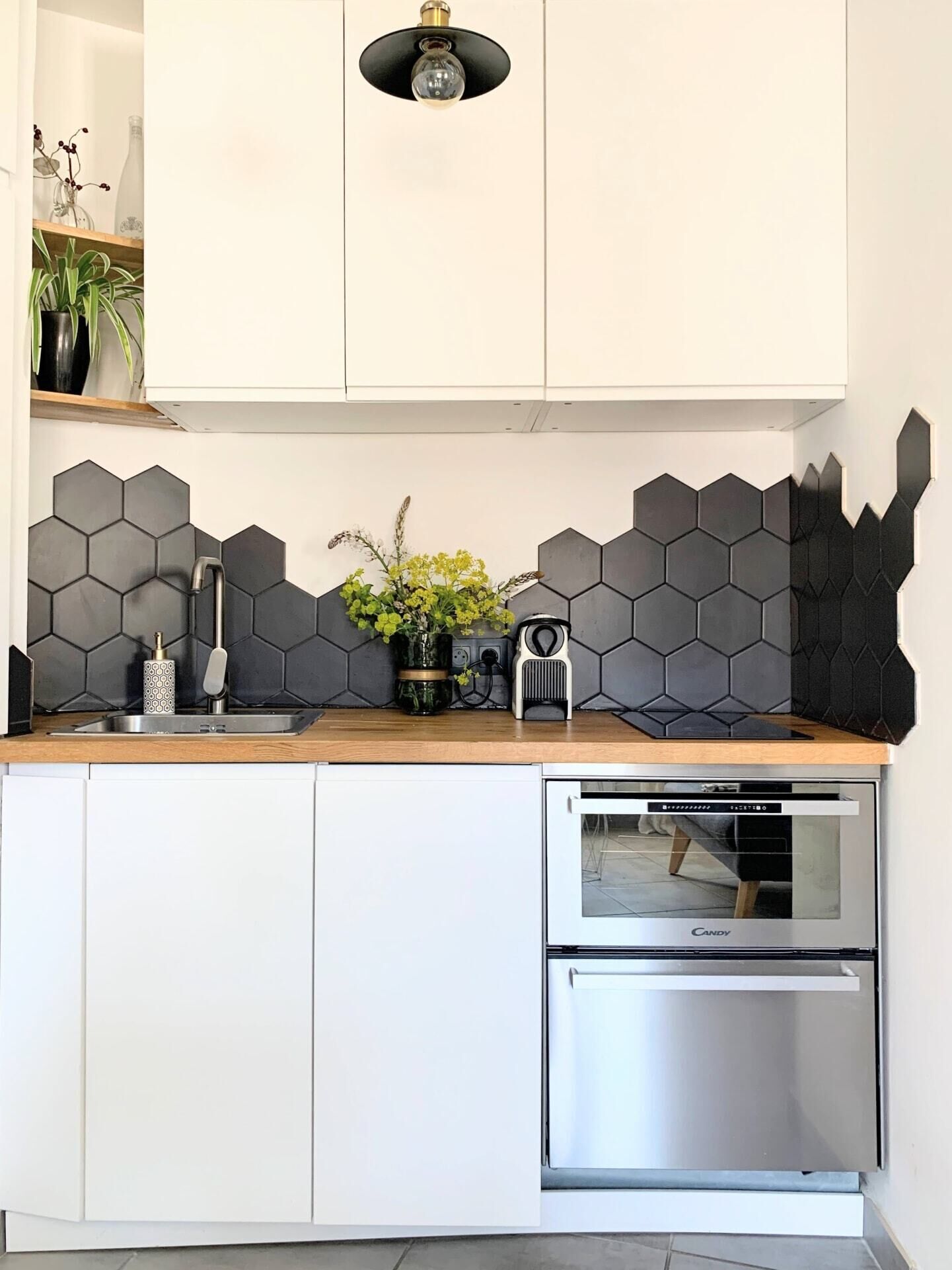 A modern kitchen with white cabinets, a stainless steel oven, and a black hexagonal backsplash.