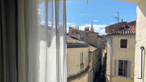 A narrow street between buildings with traditional architecture, visible through a window with sheer curtains. - Home Chic Home Les Toits de l'Argenterie (Montpellier)