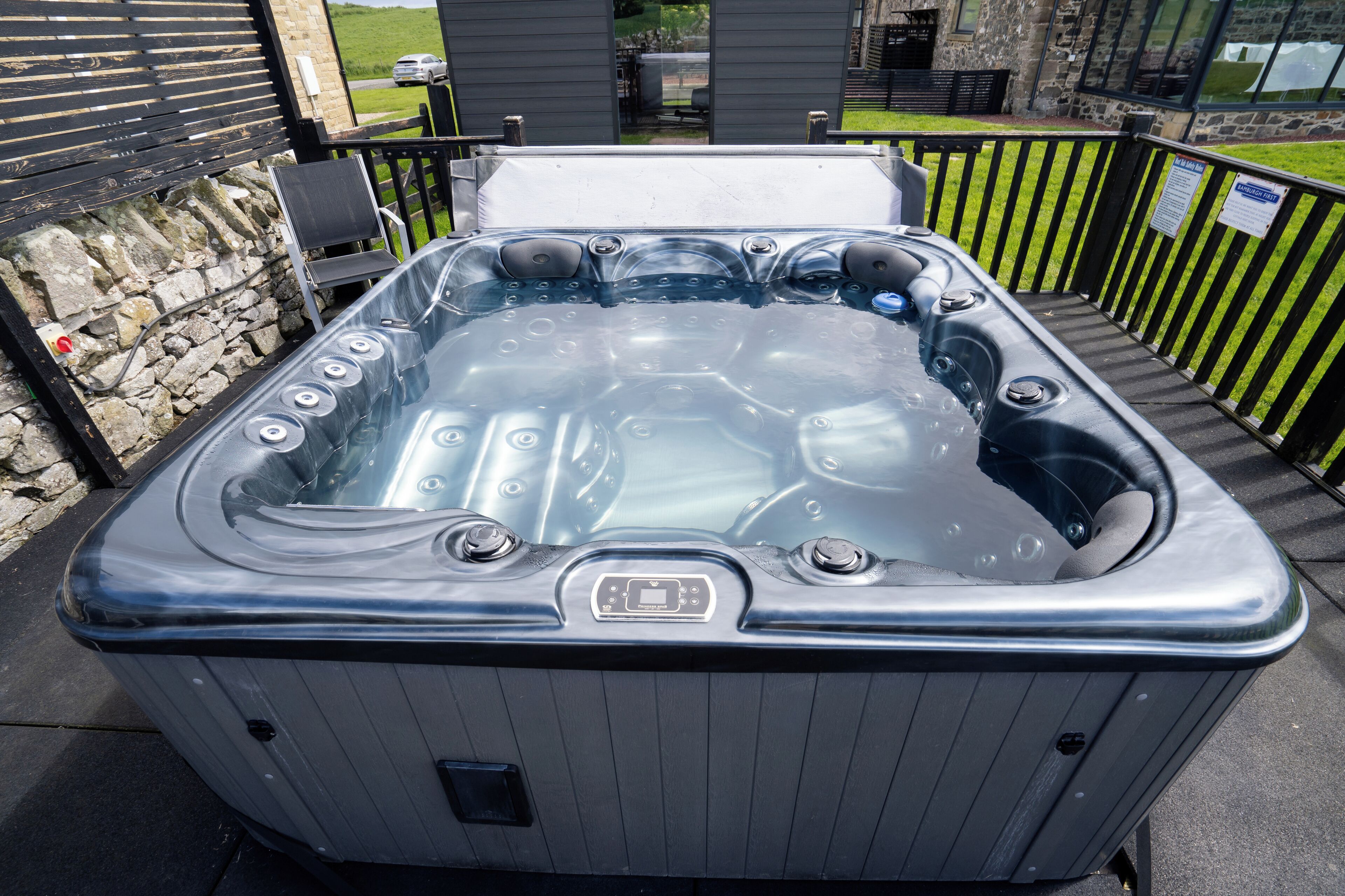 Un jacuzzi con panel de control, rodeado de muros de piedra y una valla de madera.