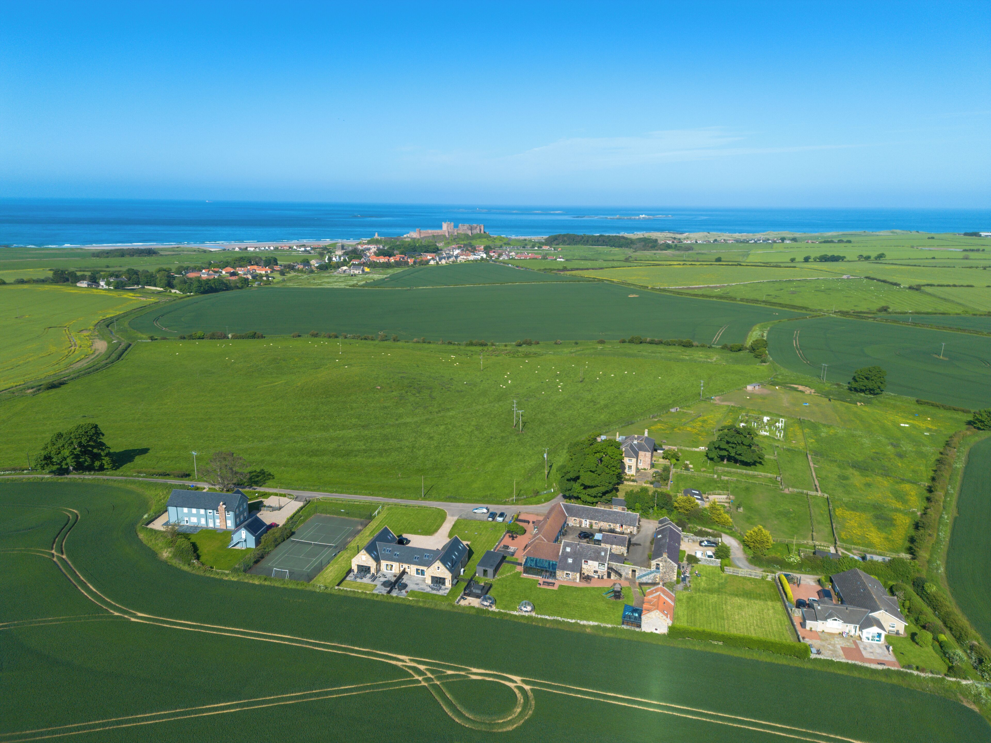 An aerial view of a rural area with fields, a small cluster of buildings, and a distant castle.