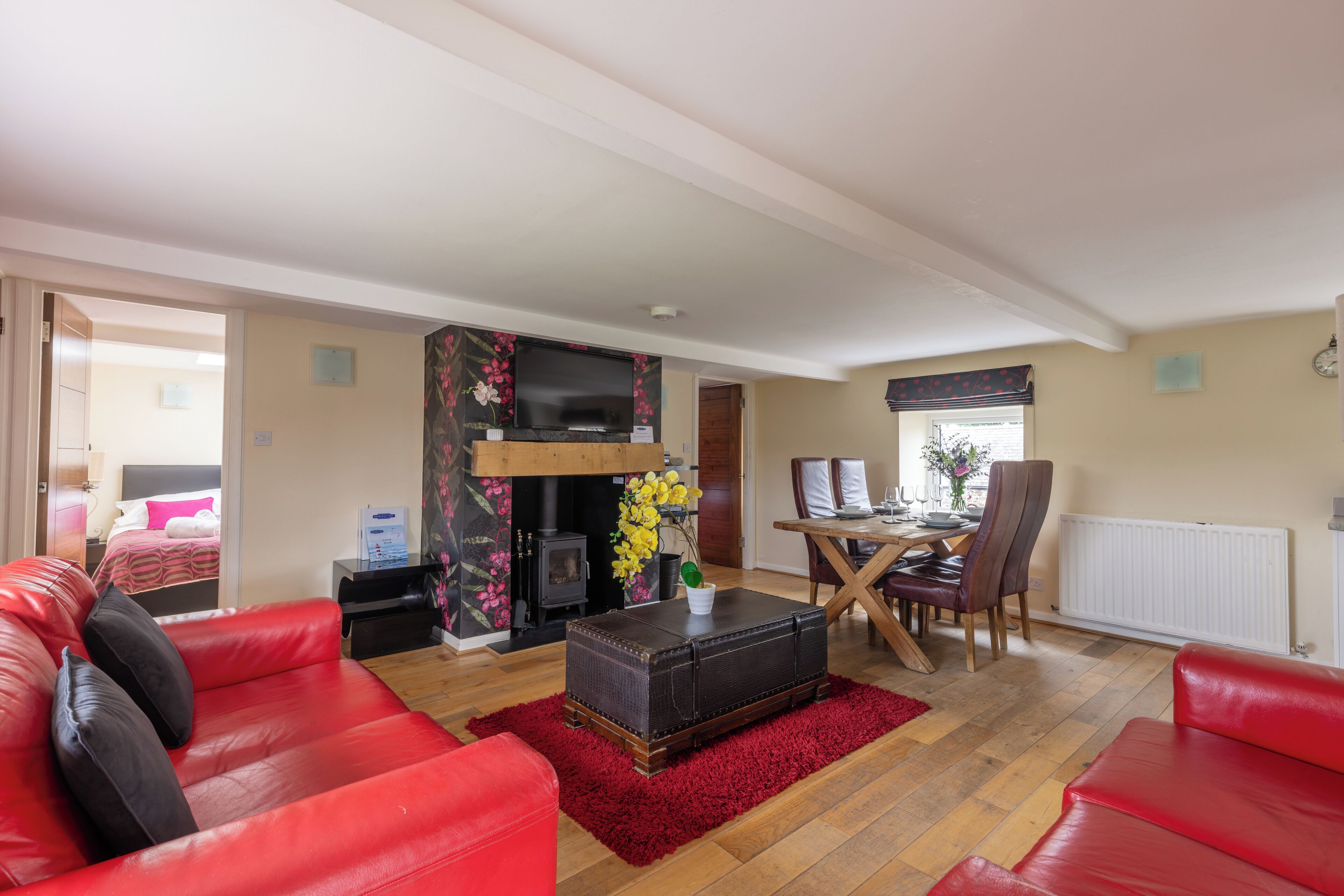 A living room with red leather sofas, a wooden coffee table, a fireplace, a TV, and a dining area with a table and chairs.