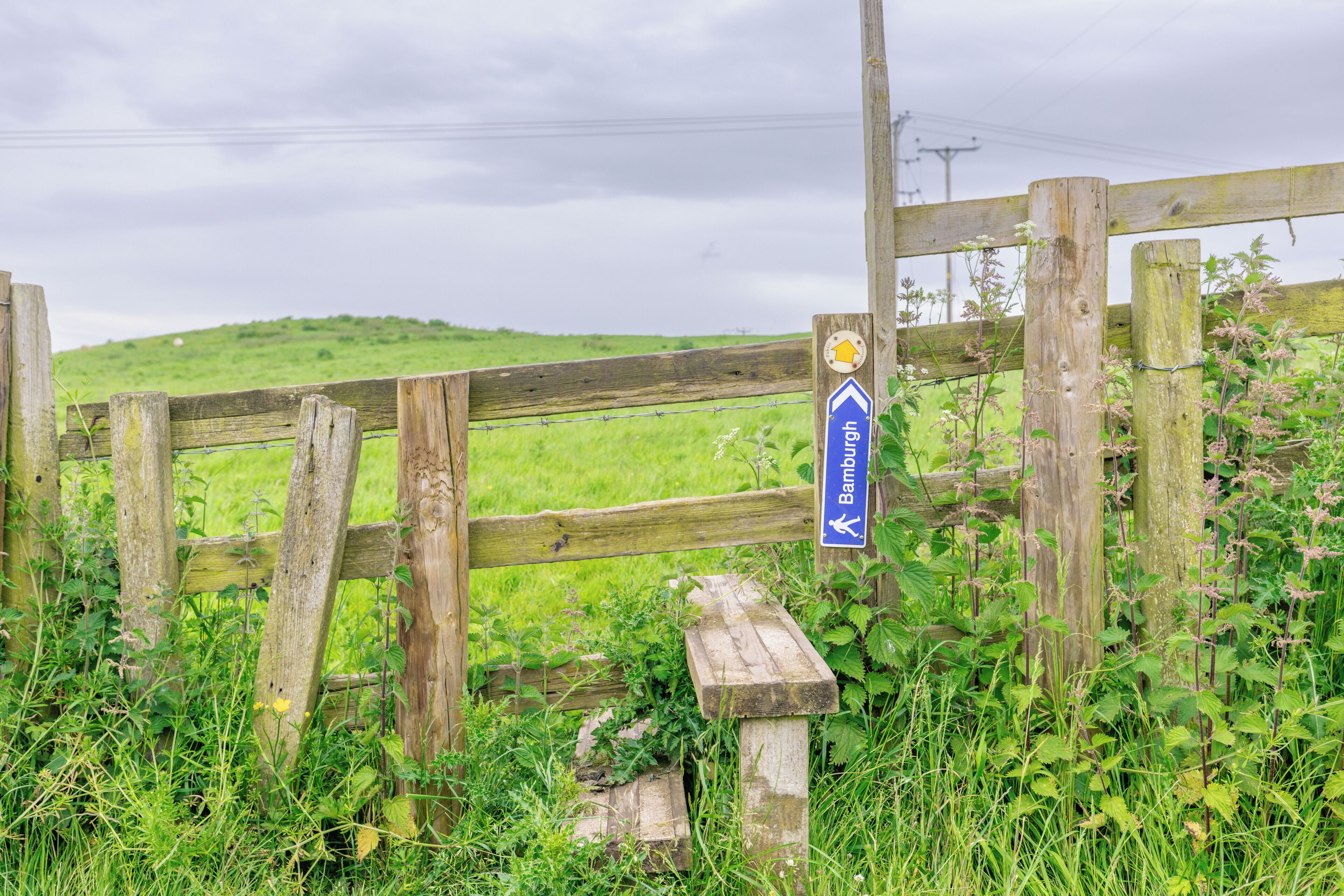 A wooden gate with a directional sign pointing towards Bamburgh.