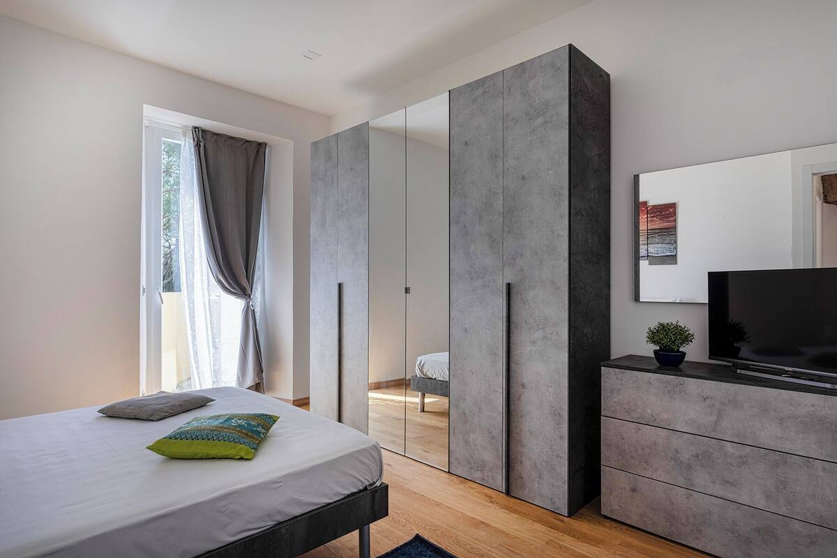 A modern bedroom with a bed, a TV, a dresser, and a large mirror.