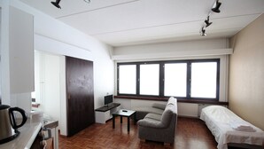 A compact room with a kitchenette, a sofa, a single bed, and a large window providing natural light. - Forenom Apartments Rauhankatu 16 (Lahti)