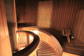 A spiral wooden staircase in a sauna room with a wooden bench and a metal container on the floor. - Forenom Apartments Rauhankatu 16 (Lahti)