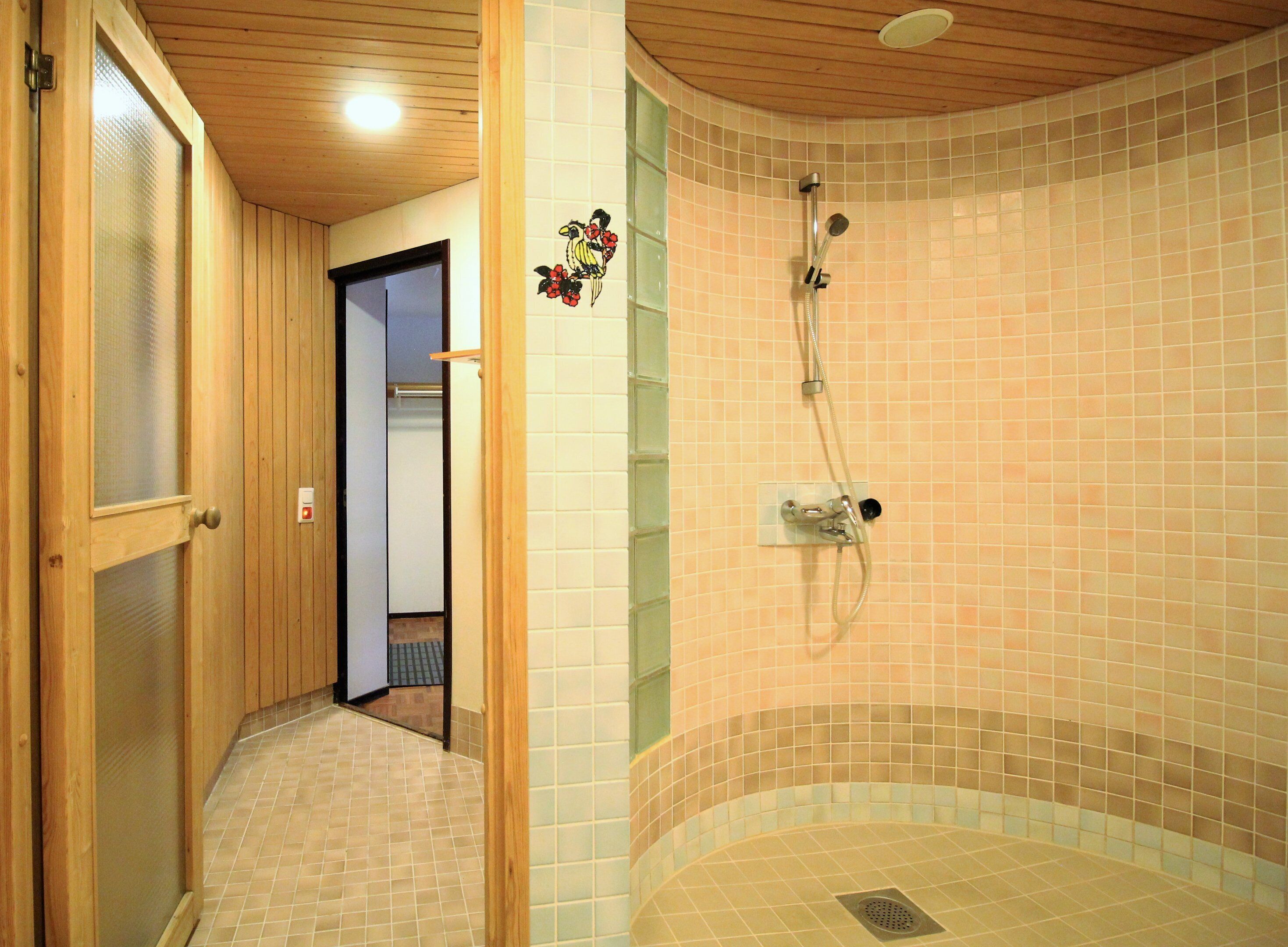 A wooden interior hallway leading to a bathroom with a shower area, tiled walls, and a visible drain.
