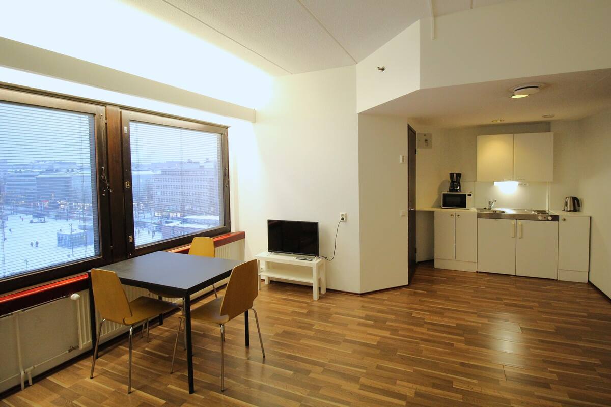 Un espacio habitable compacto con comedor, una kitchenette pequeña y un amplio ventanal con vistas a la ciudad.