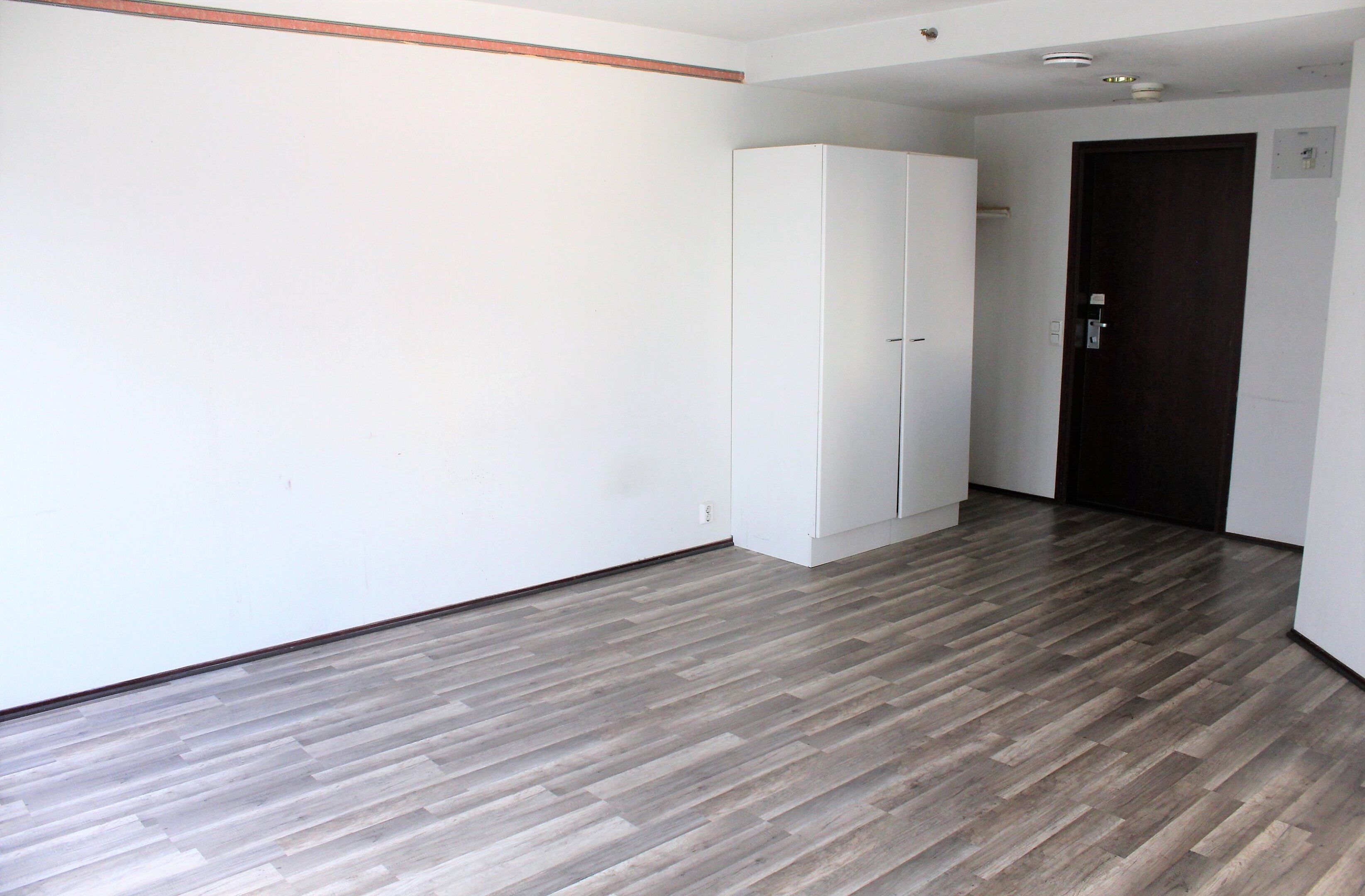 Una habitación con piso de madera, paredes blancas y un armario.