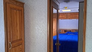A bedroom with a wooden wardrobe, a bed with a blue bedspread, and a mirror reflecting the room.