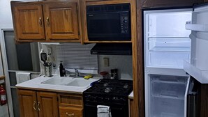 A compact kitchen with wooden cabinets, a microwave, a stove, and a refrigerator.